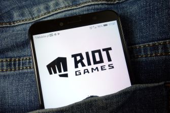 A smartphone displaying the Riot Games logo, partially hidden in a denim pocket.