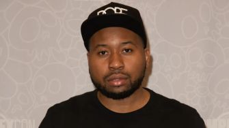 Image of DJ Akademiks at a public event, wearing a black cap and t-shirt.