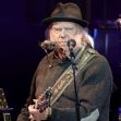 Neil Young performing on stage with a harmonica and guitar. Neil Young performing on stage with a harmonica and guitar.