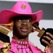 Lil Nas X holding Grammy Awards while wearing a pink cowboy hat and outfit. Lil Nas X holding Grammy Awards while wearing a pink cowboy hat and outfit.