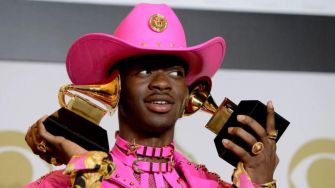 Lil Nas X holding Grammy Awards while wearing a pink cowboy hat and outfit.
