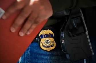 Close-up of an ICE officer's badge attached to their uniform during immigration enforcement operations.