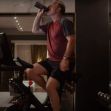 A man drinking from a water bottle while exercising on a Peloton bike in an upscale home setting. A man drinking from a water bottle while exercising on a Peloton bike in an upscale home setting.