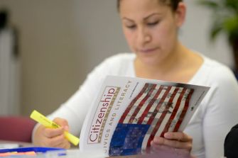A person studying a citizenship civics and literacy guide with an American flag design on the cover.
