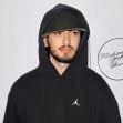Blanket Jackson at an event, wearing a black hoodie and cap, with a logo featuring Michael Jackson's signature in the background. Blanket Jackson at an event, wearing a black hoodie and cap, with a logo featuring Michael Jackson's signature in the background.