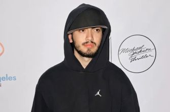 Blanket Jackson at an event, wearing a black hoodie and cap, with a logo featuring Michael Jackson's signature in the background.