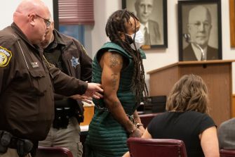 Darrell Brooks appears in court, flanked by law enforcement officers, facing multiple charges related to a deadly incident at a Wisconsin holiday parade.