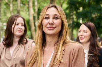 A group of women outdoors, with one woman in the foreground appearing confident and composed, while two others stand slightly behind her.