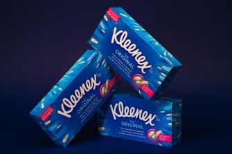 Stacked boxes of Kleenex tissues in bright blue packaging against a dark background.