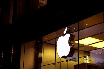 Apple logo illuminated at night on a store facade.