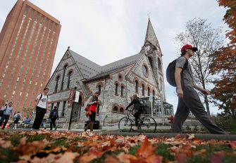 UMass campus scene with students walking and biking past a historic building during autumn.