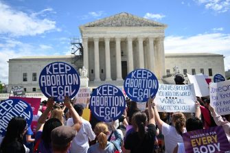 A crowd holding signs that say "KEEP ABORTION LEGAL" in front of a large building, likely a courthouse, during a protest.