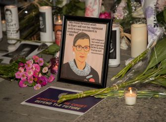 A memorial display for Justice Ruth Bader Ginsburg, featuring a framed portrait, flowers, and candles, with a quote reflecting her wish for a new president before her replacement.