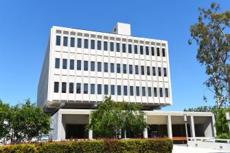 A modern university building with a blue sky and greenery in the foreground.