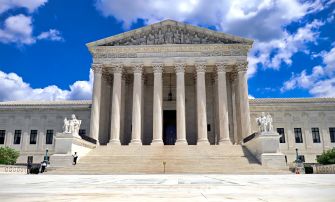 Exterior view of the United States Supreme Court building with a clear blue sky and clouds.