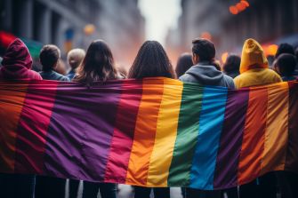 A group of individuals holding a large rainbow flag during a demonstration or march, symbolizing LGBTQ+ pride and solidarity.