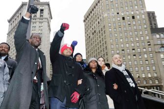 A group of individuals raising their fists in solidarity, possibly advocating for social justice, in an urban environment.