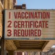 Signboard displaying text: "1. VACCINATION 2. CERTIFICATE 3. REQUIRED." Signboard displaying text: "1. VACCINATION 2. CERTIFICATE 3. REQUIRED."