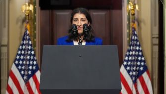 Lina Khan, FTC Chair, speaking at a podium with American flags in the background.