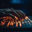 Hands typing on a backlit keyboard, representing cybersecurity and potential data breach scenarios. Hands typing on a backlit keyboard, representing cybersecurity and potential data breach scenarios.