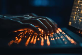 Hands typing on a backlit keyboard, representing cybersecurity and potential data breach scenarios.