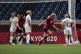 A scene from a women's soccer match, showing players from both teams near the goal area.