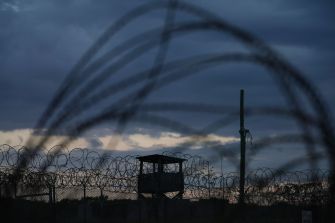 View of a guard tower surrounded by barbed wire at the Guantanamo Bay detention facility during dusk.