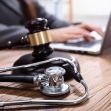 A gavel and stethoscope on a table, with a person using a laptop in the background, symbolizing medical malpractice law and legal processes. A gavel and stethoscope on a table, with a person using a laptop in the background, symbolizing medical malpractice law and legal processes.