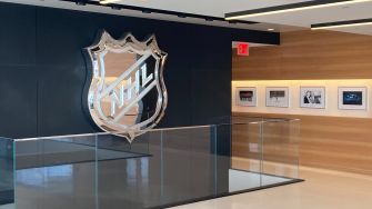 NHL logo displayed in the lobby area of the NHL headquarters, featuring a modern design with a glass railing and framed photographs on the wall.