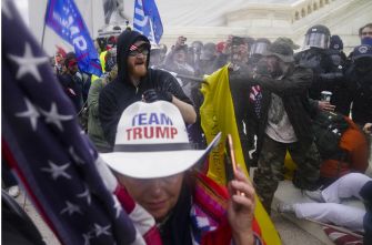 A crowd of protesters at the Capitol during the riots, with one individual wearing a "TEAM TRUMP" hat in the foreground.