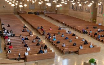 A nearly empty church interior with a few congregants seated in the pews, observing social distancing measures.
