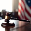 Gavel on a table with an American flag in the background, symbolizing a courtroom setting. Gavel on a table with an American flag in the background, symbolizing a courtroom setting.