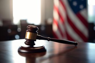 Gavel on a table with an American flag in the background, symbolizing a courtroom setting.