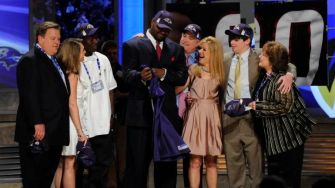 Michael Oher at the NFL draft ceremony surrounded by family and supporters, holding Ravens gear.