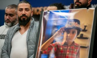 A man stands beside a poster of his deceased son, Wadea Al-Fayoume, during a press conference regarding a wrongful death lawsuit following the boy's murder.