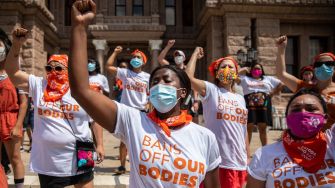 A group of protesters wearing masks and shirts with the slogan "BANS OFF OUR BODIES" raise their fists in a demonstration against the Texas abortion law.