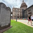 Monument displaying the Ten Commandments in front of a government building, with pedestrians walking by. Monument displaying the Ten Commandments in front of a government building, with pedestrians walking by.