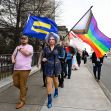 A diverse group of people, including a drag performer, marching with LGBTQ+ flags in a demonstration. A diverse group of people, including a drag performer, marching with LGBTQ+ flags in a demonstration.