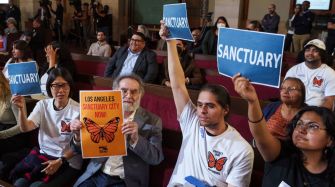 A group of supporters holding signs advocating for Los Angeles to be a sanctuary city during a city council meeting.