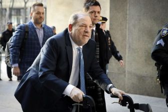 Harvey Weinstein arriving in court using a walker, flanked by two individuals.