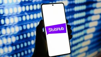 A person holding a smartphone displaying the StubHub logo against a blurred blue background.