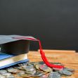 A graduation cap resting on a stack of coins next to a book, symbolizing student debt and education finances. A graduation cap resting on a stack of coins next to a book, symbolizing student debt and education finances.