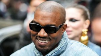 Kanye West wearing sunglasses and smiling, surrounded by a crowd.