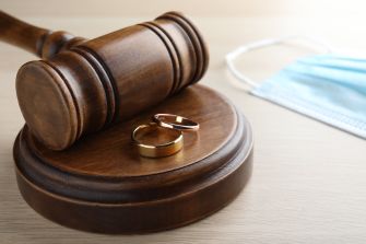 A gavel, wedding rings, and a face mask arranged on a table, symbolizing marriage and divorce during the COVID-19 pandemic.