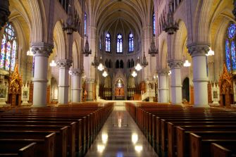 Interior view of a large church with ornate architecture, stained glass windows, and rows of empty pews.