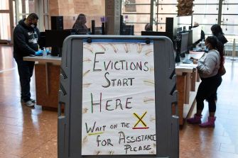 Sign indicating the start of evictions and requesting individuals to wait for assistance, with people working in the background.