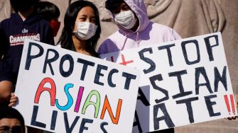 Two individuals holding protest signs that read "Protect Asian Lives" and "Stop Asian Hate" at a rally.