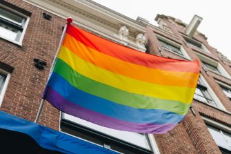 A rainbow flag waving in front of a brick building.