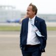 A man in a suit walking on an airport tarmac, appearing contemplative. A man in a suit walking on an airport tarmac, appearing contemplative.