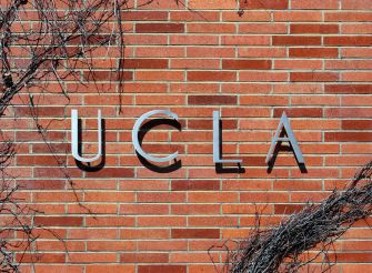 Sign displaying "UCLA" on a brick wall, with vines partially covering the area.